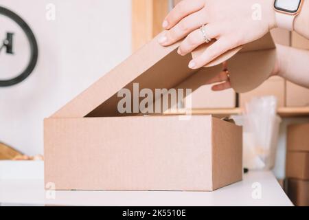 Photo rognée des mains de la femme qui emballe, préparant le colis pour la livraison aux clients. Propriétaire de petite entreprise, entrepreneur individuel dans l'atelier Banque D'Images