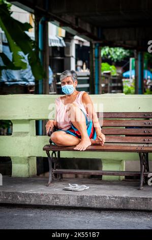 Une femme thaïlandaise portant un masque de protection regarde la vie passer dans les rues étroites et les ruelles de la région de Ruamrudee près de Lumpini Park Bangkok Thaïlande. Banque D'Images