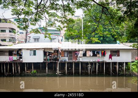 Les vieilles maisons traditionnelles thaïlandaises sur pilotis au-dessus d'une rivière contrastent avec les gratte-ciel modernes dans la communauté de Soi Ruamrudee, Bangkok, Thaïlande. Banque D'Images