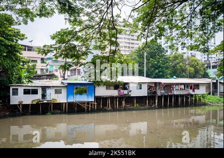 Les vieilles maisons traditionnelles thaïlandaises sur pilotis au-dessus d'une rivière contrastent avec les gratte-ciel modernes dans la communauté de Soi Ruamrudee, Bangkok, Thaïlande. Banque D'Images