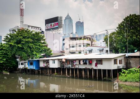 Les vieilles maisons traditionnelles thaïlandaises sur pilotis au-dessus d'une rivière contrastent avec les gratte-ciel modernes dans la communauté de Soi Ruamrudee, Bangkok, Thaïlande. Banque D'Images