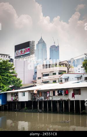 Les vieilles maisons traditionnelles thaïlandaises sur pilotis au-dessus d'une rivière contrastent avec les gratte-ciel modernes dans la communauté de Soi Ruamrudee, Bangkok, Thaïlande. Banque D'Images