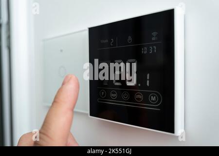 Gros plan d'une main mâle qui règle un thermostat numérique moderne fixé au mur. Température confortable de la pièce à 20 degrés Celsius. Thermomètre électronique activé Banque D'Images