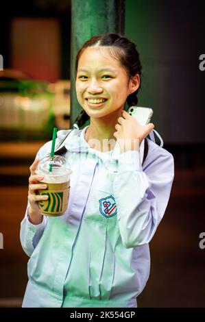 Une belle fille d'école thaïlandaise pose et rit en tenant sa boisson Starbucks attendant un bus à Sala Daeng, Bangkok, Thaïlande. Banque D'Images