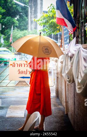 Un moine thaïlandais abrite sous un parapluie pendant une douche à la pluie au temple thaïlandais Wat Paknam Bhasicharon où se trouve l'immense bouddha doré. Bangkok. Banque D'Images