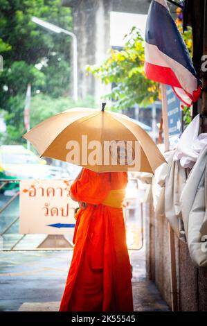 Un moine thaïlandais abrite sous un parapluie pendant une douche à la pluie au temple thaïlandais Wat Paknam Bhasicharon où se trouve l'immense bouddha doré. Bangkok. Banque D'Images