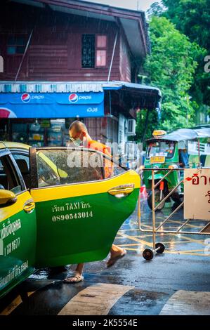 Un moine thaïlandais entre dans un taxi pendant une douche de pluie au temple thaïlandais Wat Paknam Bhasicharon où se trouve l'immense bouddha doré. Bangkok Thaïlande. Banque D'Images