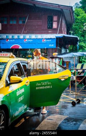 Un moine thaïlandais entre dans un taxi pendant une douche de pluie au temple thaïlandais Wat Paknam Bhasicharon où se trouve l'immense bouddha doré. Bangkok Thaïlande. Banque D'Images