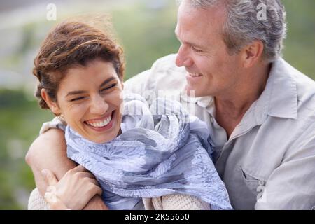 Ils trouvent toujours le temps de rire. Un couple mûr riant et embrassant tout en appréciant une journée dans la nature. Banque D'Images