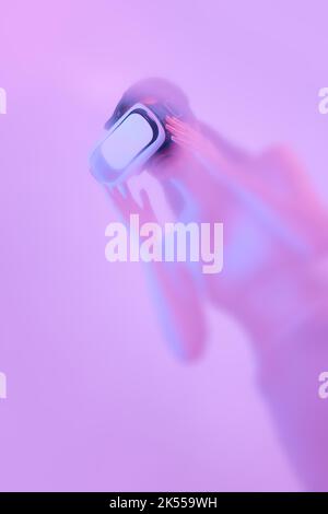 Modèle femelle en lunettes de réalité virtuelle, immergé dans les nuages de fumée, brouillard sur fond rose fluo avec un diffuseur de rétroéclairage. Banque D'Images