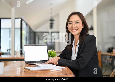 Une femme d'affaires ou une comptable asiatique du millénaire, attirante et professionnelle, portant des lunettes, est assise à son bureau avec un écran vierge d'ordinateur portable Banque D'Images