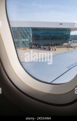 Vue depuis la fenêtre d'un avion à un aéroport, avec une file d'attente de personnes dans la distance de départ pour leur avion. Banque D'Images