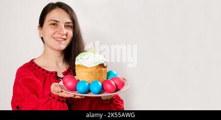 Une femme tient un gâteau de Pâques et peint des oeufs sur un fond blanc, bannière avec place pour le texte. Banque D'Images