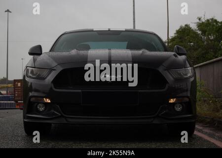 La Mustang GT De Ford A 2015 noir brillant avec roues en alliage noir brillant et bandes de course gris dégradé à travers le capot sur une zone industrielle Banque D'Images