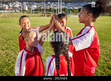 Les enfants, l'équipe de football des filles et les cinq hauts pour la motivation de groupe sportif sur un terrain de football pour célébrer le but, la victoire et le travail d'équipe en plein air Banque D'Images