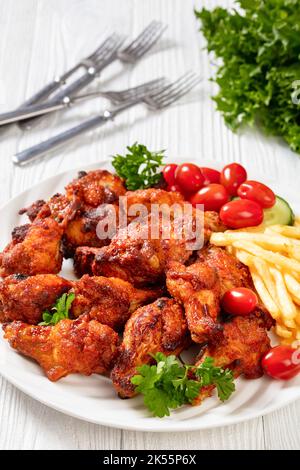 ailes de poulet grillées croustillantes avec frites, tomates, concombre, persil sur plaque blanche sur table en bois blanc, vue verticale depuis le dessus Banque D'Images
