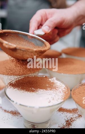 Le processus de préparation du dessert tiramisu. Le plat est arrosé de cacao à travers un tamis. Gros plan, mise au point sélective. Banque D'Images