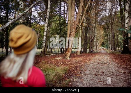 Jeune femme en blouson rouge marchant dans la forêt Banque D'Images