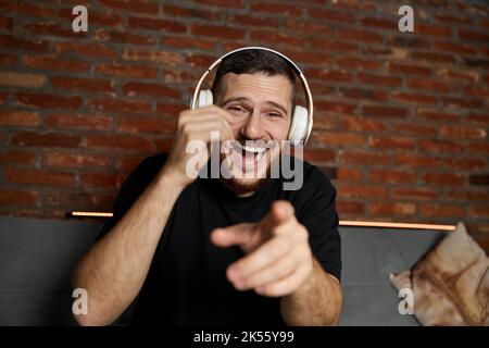 Beau barbu dans un casque qui écoute de la musique à la maison. Musique. Portrait en demi-longueur d'un jeune homme souriant dans des vêtements décontractés de style jeune assis Banque D'Images