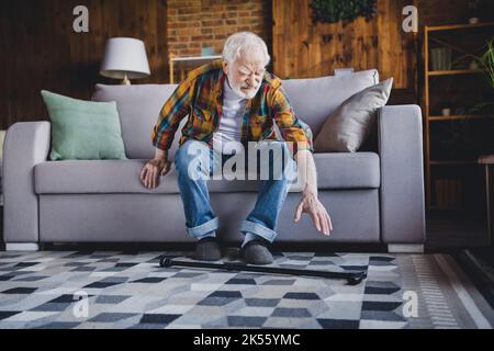 Photo de l'homme solitaire fatigué pensionné porter une chemise à carreaux essayer de se lever un canapé tomber canne à pied à l'intérieur de la maison Banque D'Images