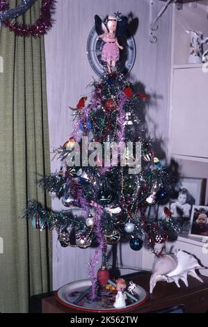 Un sapin de Noël artificiel de 1970s avec des décorations dans un salon familial au-dessus d'un téléviseur, Londres, Royaume-Uni Banque D'Images