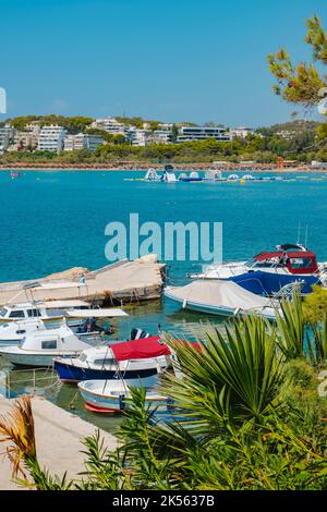 Vue sur un petit port de Vouliagmeni, Grèce, avec quelques bateaux amarrés en elle et la plage de Vouliagmeni en arrière-plan Banque D'Images