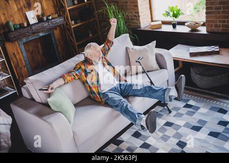 Photo de l'homme excité réussi retraité porter une chemise à carreaux regarder match les poings montant assis canapé à l'intérieur de la maison Banque D'Images