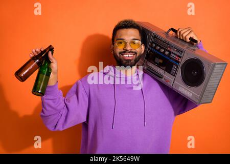 Portrait de l'homme insouciant et joyeux porte-boombox tenir les bouteilles de bière isolées sur fond de couleur orange Banque D'Images