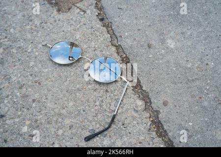 Lunettes de soleil rondes brisées sur un sol en béton Banque D'Images