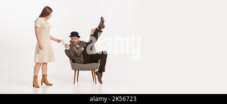 Portrait d'un homme en costume, chapeau avec moustaches assis sur une chaise sur fond blanc. Femme lui versant du café Banque D'Images