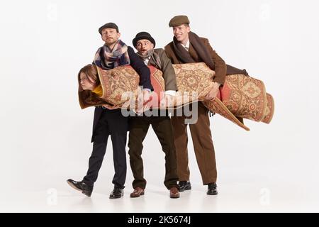 Image amusante de trois hommes élégants portant une jeune femme recouverte de moquette sur fond blanc Banque D'Images