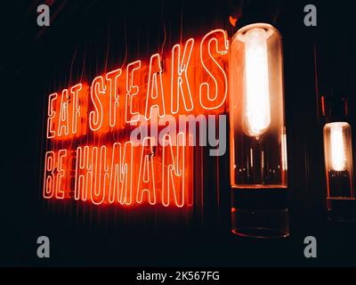 Gros plan sur un éclairage au néon rouge avec inscription « Eat steaks be Human » et lampes vintage dans le noir. Banque D'Images