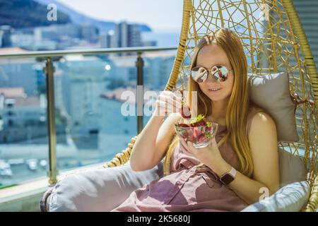 Portrait d'une femme magnifique portant une belle robe assise dans un patio et mangeant de la fraise Banque D'Images