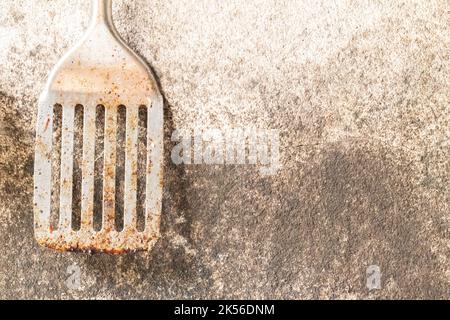 Vieille spatule à poisson rouillée et corrodée sur fond de mur sale. Banque D'Images