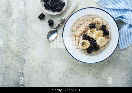 Flocons d'avoine. Bol de porridge de flocons d'avoine avec des graines de mûre, de banane et de chia sur fond de table vieux en béton gris. Vue de dessus en style de pose à plat. Naturel i Banque D'Images