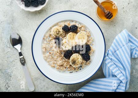 Flocons d'avoine. Bol de porridge de flocons d'avoine avec des graines de mûre, de banane et de chia sur fond de table vieux en béton gris. Vue de dessus en style de pose à plat. Naturel i Banque D'Images