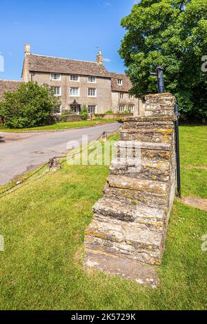 Une pompe à eau en fonte sur un grand bloc de montage en pierre sur le green dans le village de Cotswold de Meysey Hampton, Gloucestershire, Angleterre Royaume-Uni Banque D'Images