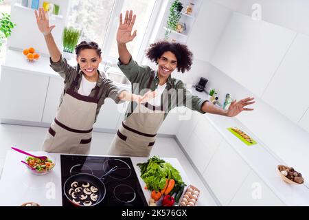 Portrait de deux partenaires positifs amusants lever les mains palmiers vague bonjour salutations ustensiles de cuisine à l'intérieur Banque D'Images