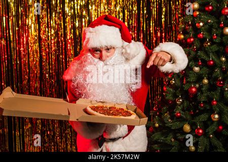 Père noël montrant une pizza à emporter dans une boîte près de la guirlande festive, image de stock Banque D'Images