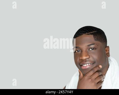 Bel homme noir. Toilettage matinal. Soins du visage. Style élégant. Joyeux homme africain confiant serviette blanche épaule en admirant lui-même touchant face isola Banque D'Images