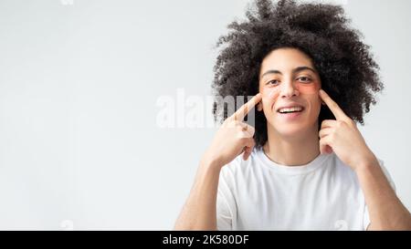 Soin de la peau pour homme. Procédure anti-âge. Traitement hydratant. Heureux satisfait beau gars avec les cheveux bruns bouclés pointant vers les timbres roses d'oeil hydrogel o Banque D'Images