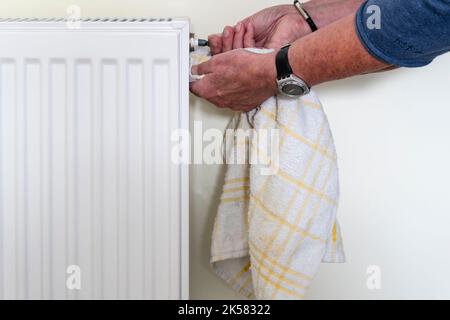 Purge de la soupape du radiateur pour évacuer l'air emprisonné et garantir le bon fonctionnement du système de chauffage central. Un chiffon est maintenu pour recueillir l'eau qui s'en est libérée. Banque D'Images