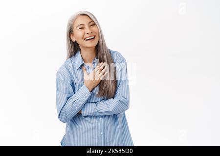 Bonne femme coréenne senior, femme asiatique d'âge moyen riant et souriant, regardant sans souci, se tenant sur fond blanc et regardant smth drôle Banque D'Images