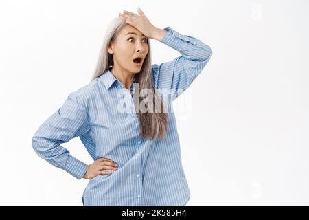 Portrait d'une femme âgée troublée qui claque le front, qui a l'air bouleversé ou déçu, a oublié le smth, se tenant sur fond blanc Banque D'Images