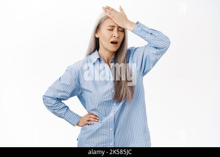 Portrait d'une femme âgée troublée qui claque le front, qui a l'air bouleversé ou déçu, a oublié le smth, se tenant sur fond blanc Banque D'Images