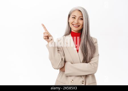 Portrait d'entrepreneur principal souriant, femme d'affaires pointant le doigt vers la gauche sur le produit, montrant une bannière publicitaire, debout sur fond blanc Banque D'Images