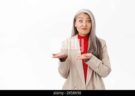 Portrait d'une femme asiatique confuse qui se hante, montrant les mains vides, levant les paumes et regardant perplexe, debout sur fond blanc Banque D'Images