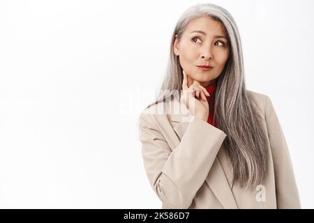 Portrait d'une femme d'affaires asiatique, d'une femme d'âge moyen qui pense, qui a l'air troublée ou perplexe, se tenant sur un fond blanc de studio Banque D'Images
