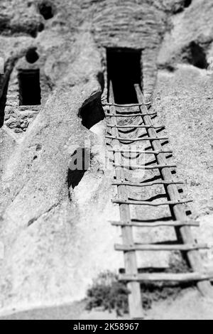 Une image en noir et blanc d'une échelle en bois mène à la porte ouverte d'une grotte du monument national de Bandelier, Nouveau-Mexique, États-Unis. Banque D'Images