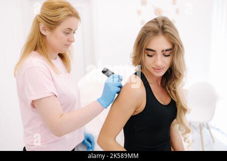 La dermatologue féminine examine les marques de naissance et les moles de la peau du patient avec un dermatoscope. Banque D'Images